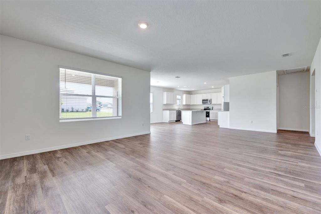 An open-concept living area features light-colored walls, wood-look flooring, and a kitchen in the background — 3610 PFEIFFER FALLS PLACE, DAVENPORT, FL