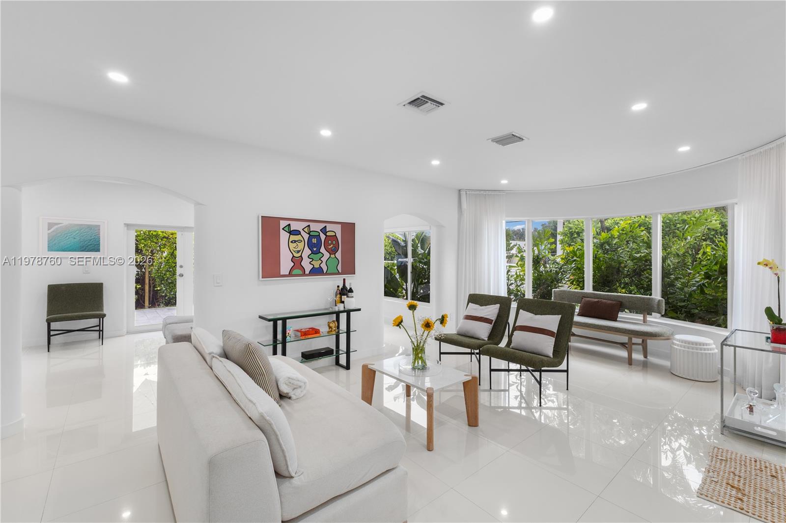 A bright living room features white tile floors, modern furniture, and large curved windows — 741 NE 87th St, Miami FL 33138, MIAMI, FL