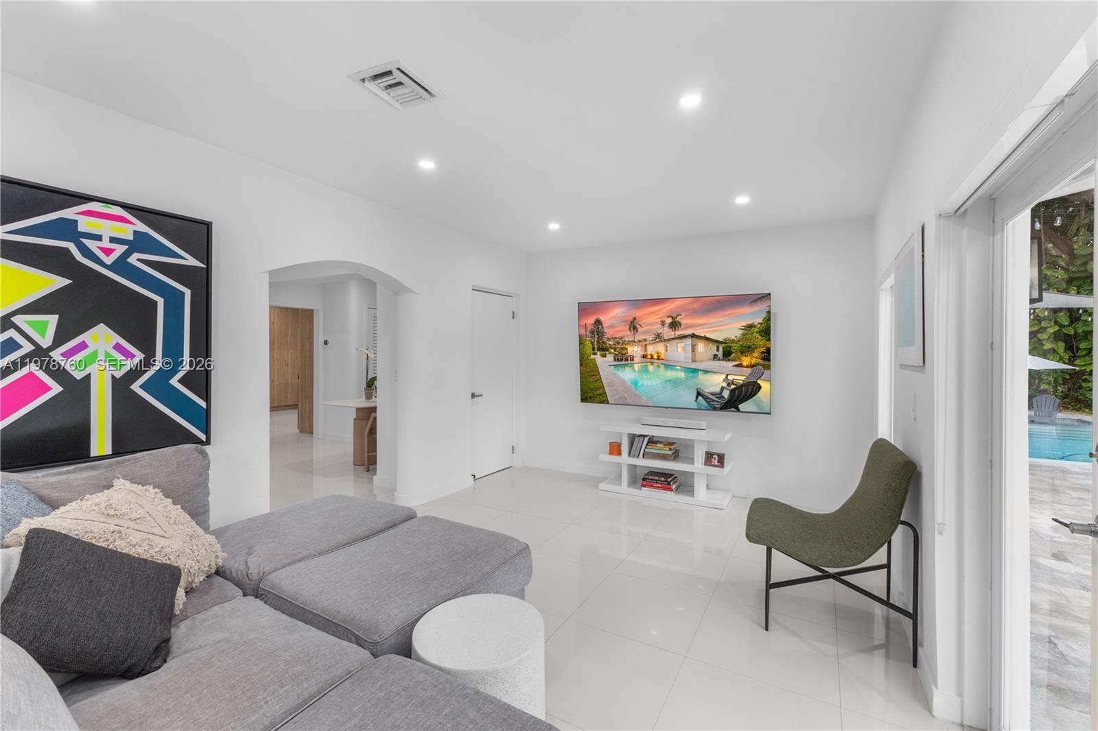 A modern living room features a gray sectional, wall-mounted television, and sliding glass doors to a pool — 741 NE 87th St, Miami FL 33138, MIAMI, FL