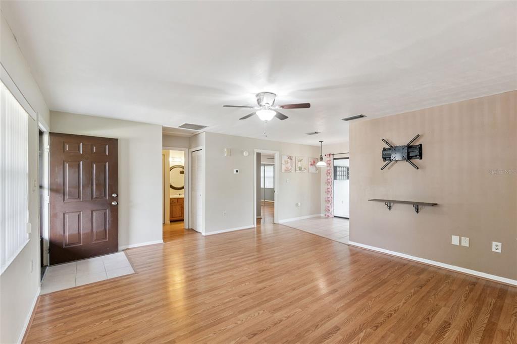 An open-concept living room features wood-look flooring, a ceiling fan, and a brown front door — 12418 ORANGEWOOD CIRCLE, TAVARES, FL