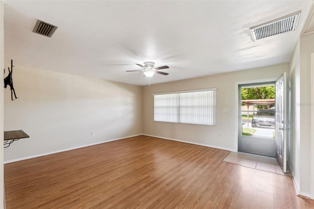An empty living room features wood-look flooring, a ceiling fan, and a glass-paneled entry door — 12418 ORANGEWOOD CIRCLE, TAVARES, FL