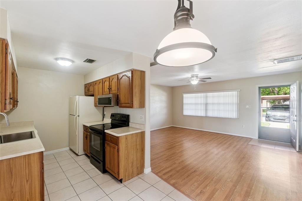 A kitchen with wood cabinets and tile floors opens into a living area with wood flooring — 12418 ORANGEWOOD CIRCLE, TAVARES, FL