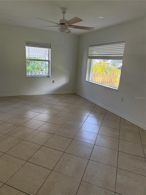 An empty room features light-colored tile flooring, white walls, a ceiling fan, and two windows — 1317 35TH AVENUE N, ST PETERSBURG, FL