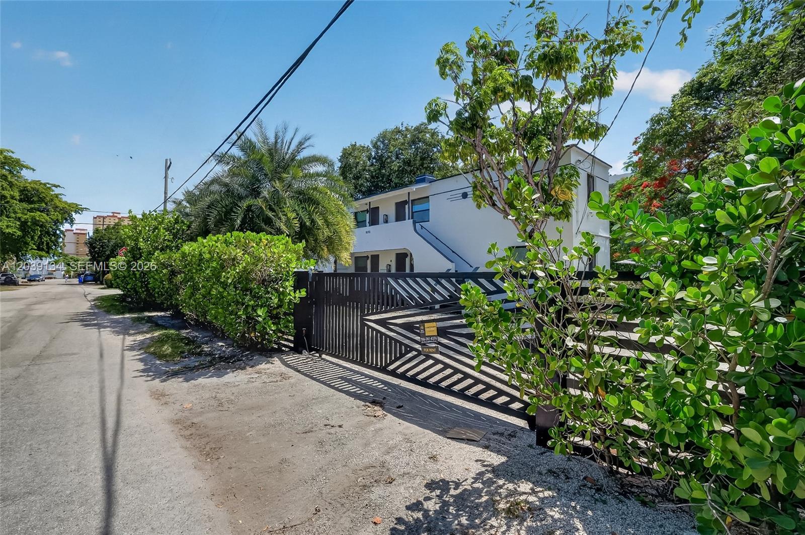 A two-story white apartment building is viewed from a street behind a black gate — 8270 NE 1st Pl # 3, Miami FL 33138, MIAMI, FL