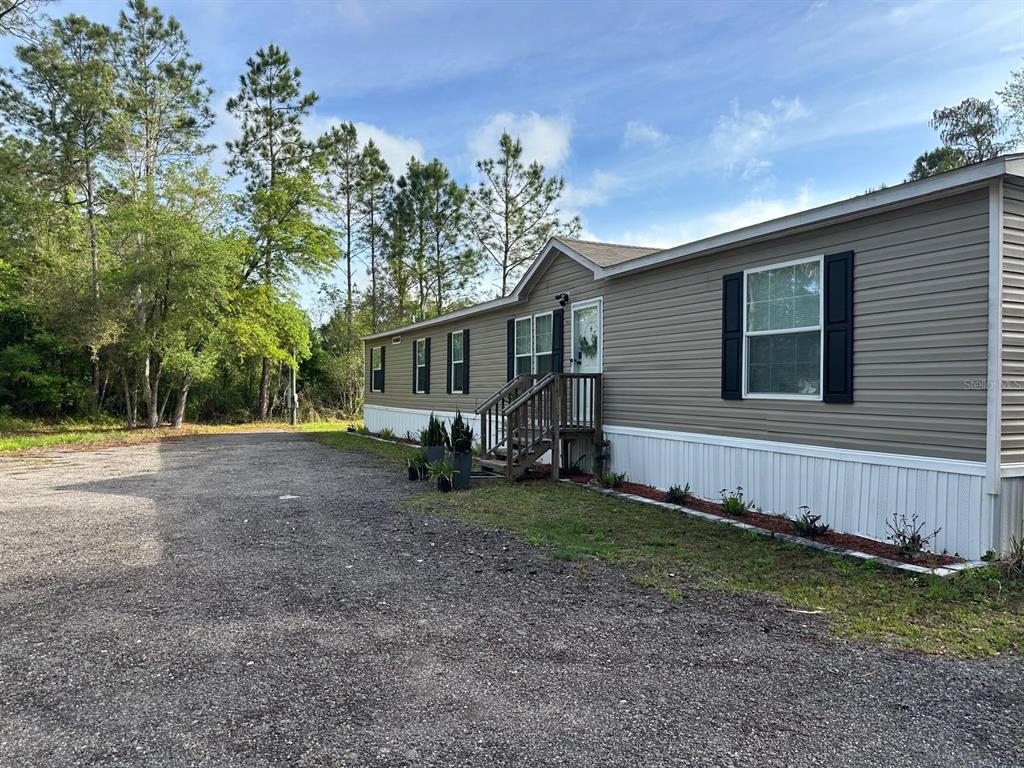 A single-story manufactured home with tan siding and a gravel driveway sits near trees — 1583 BEECH BOULEVARD, BUNNELL, FL