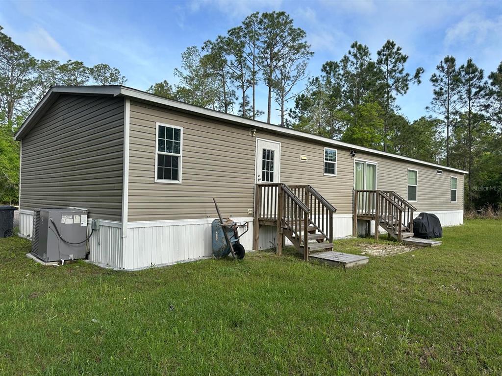 A tan mobile home with two wooden entry staircases sits on a grassy lot — 1583 BEECH BOULEVARD, BUNNELL, FL