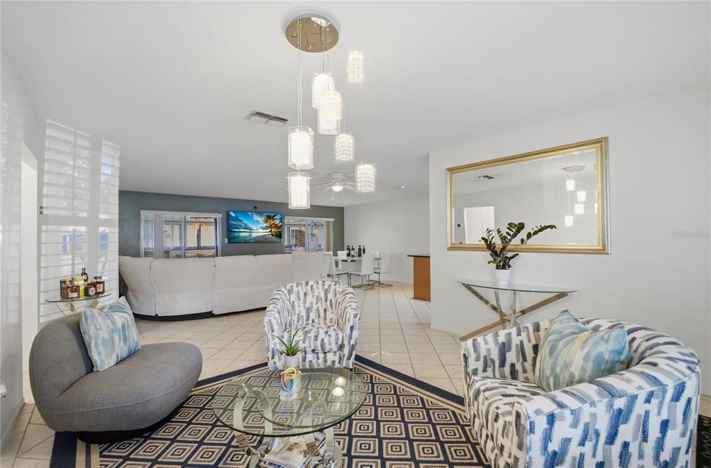 A living room features a modern chandelier, patterned armchairs, a glass coffee table, and tile flooring — 10725 WILLIAM TELL DRIVE, ORLANDO, FL