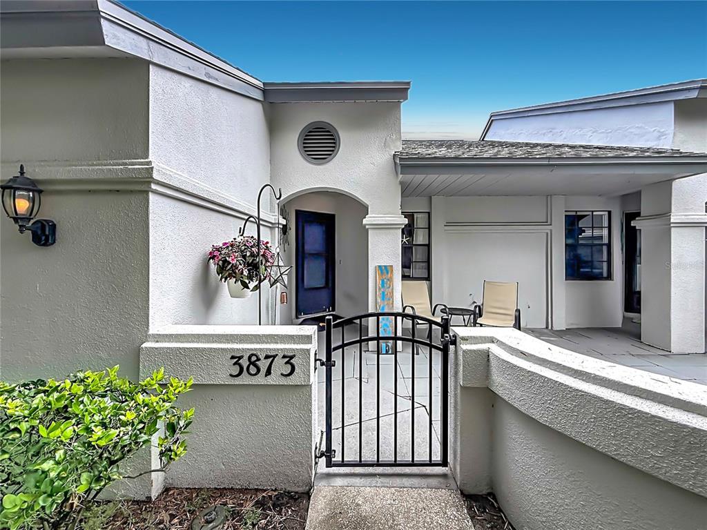 A gated courtyard entrance features a white stucco exterior, a blue door, and patio furniture — 3873 PHEASANT COURT, PALM HARBOR, FL