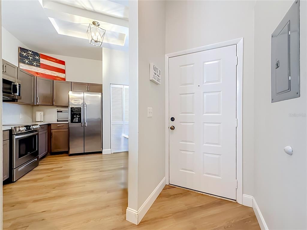 A kitchen with stainless steel appliances and wood-look flooring sits beside a white entry door — 3873 PHEASANT COURT, PALM HARBOR, FL