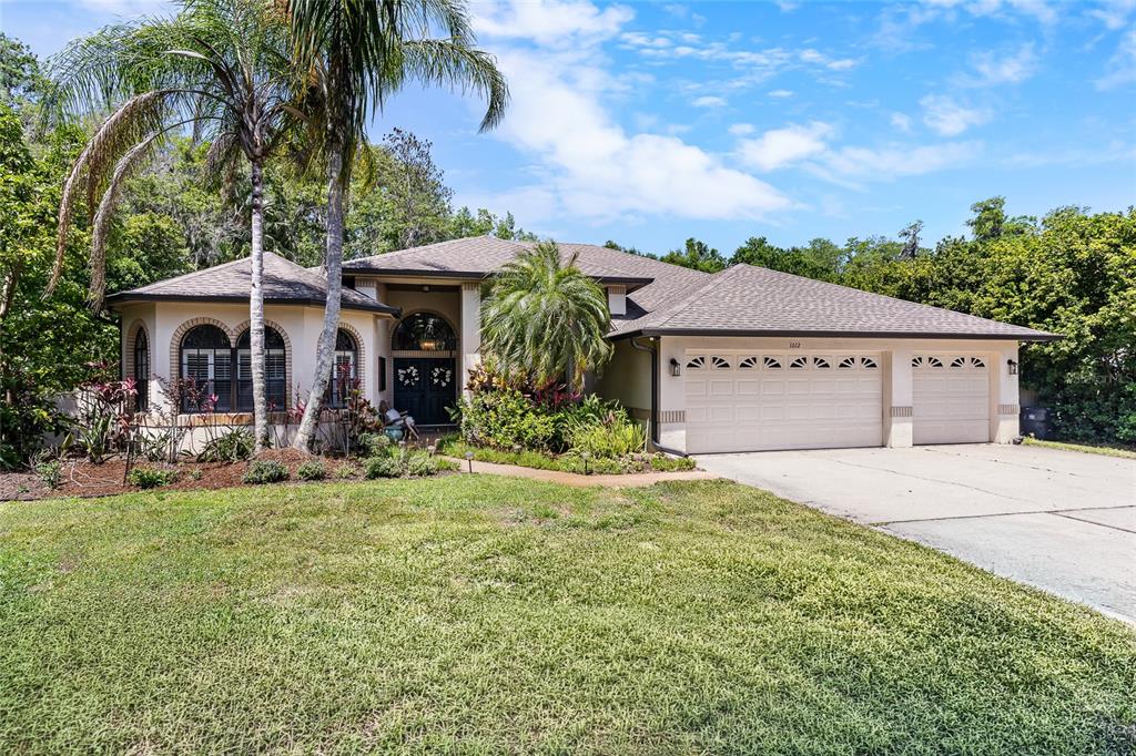 A single-story house with a three-car garage, palm trees, and a landscaped front yard — 1012 KINGSBOROUGH GARDENS COURT, LUTZ, FL
