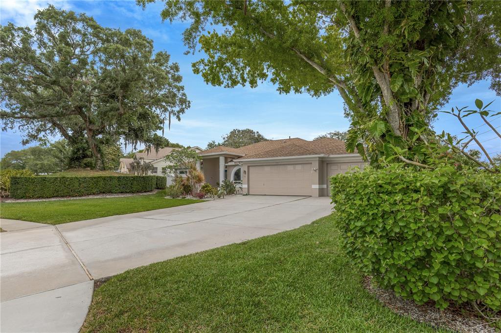 A single-story house with a beige exterior, a three-car garage, and a large front lawn — 727 HIDDEN LAKE DRIVE, TARPON SPRINGS, FL