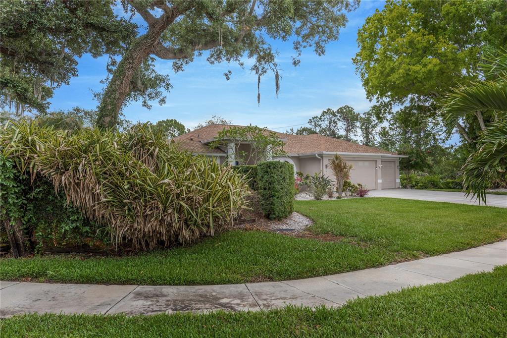 A single-story house with a tan exterior and a two-car garage sits behind landscaping — 727 HIDDEN LAKE DRIVE, TARPON SPRINGS, FL