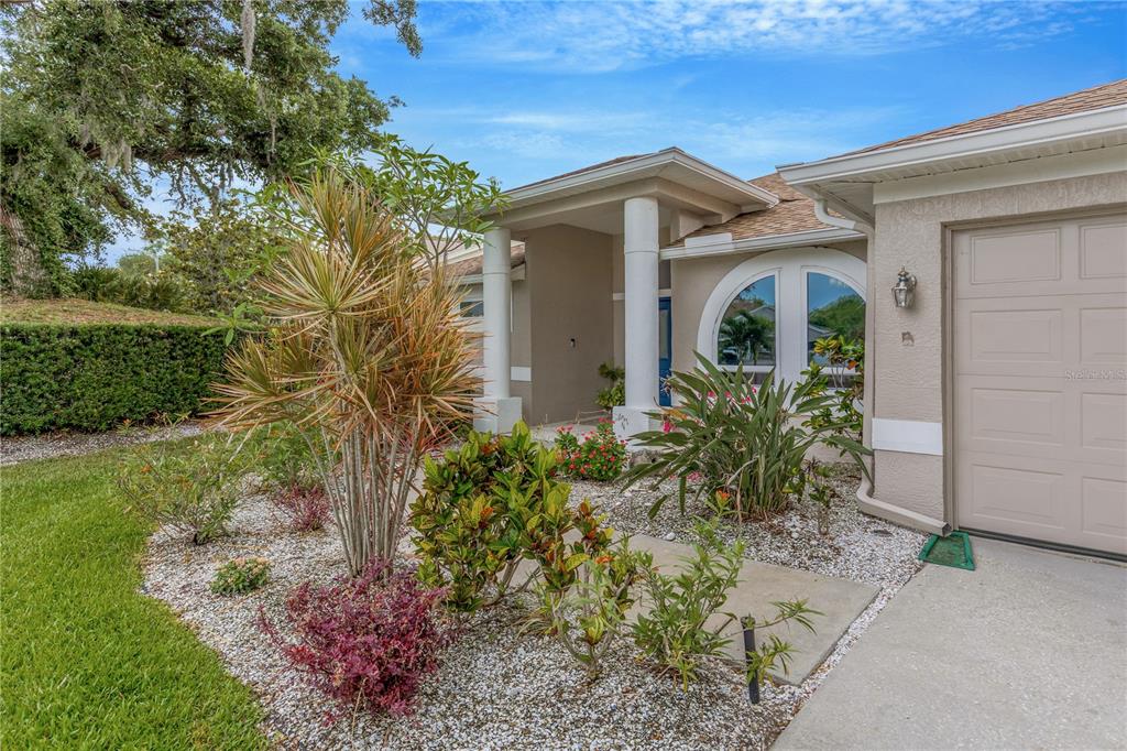 A view of a house exterior featuring a front walkway, landscaping, and a garage door — 727 HIDDEN LAKE DRIVE, TARPON SPRINGS, FL