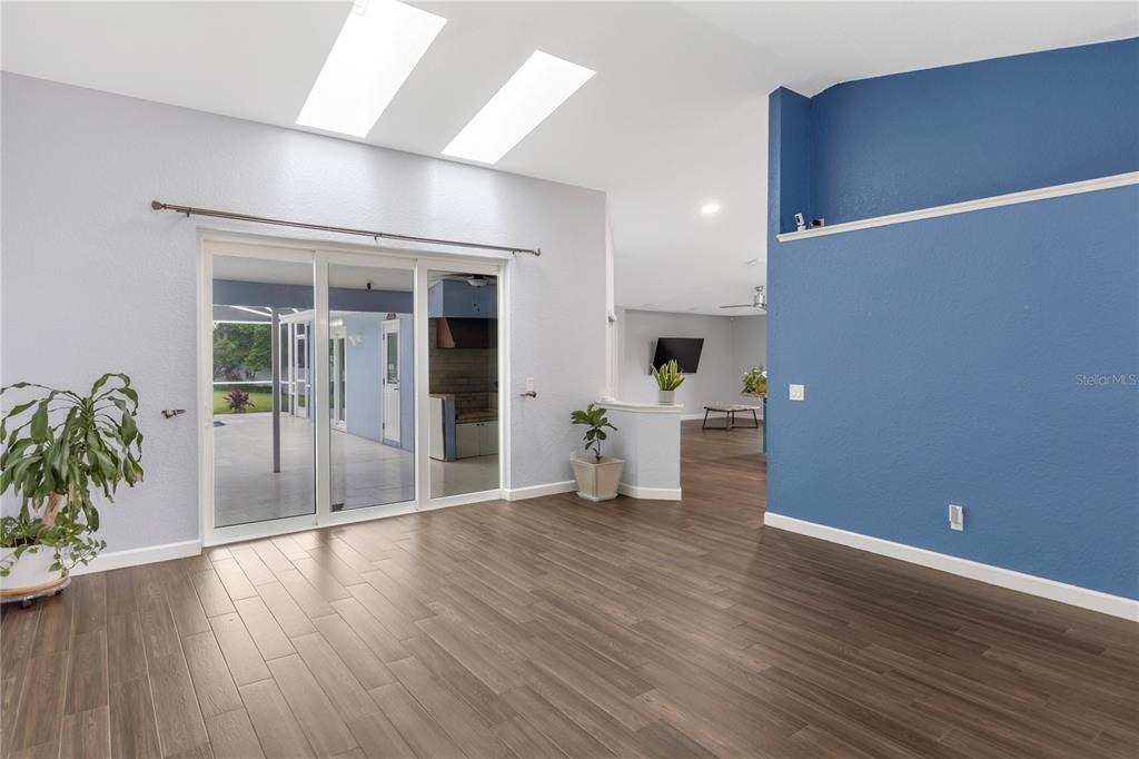 A living area features wood-look flooring, a blue accent wall, and sliding glass patio doors — 727 HIDDEN LAKE DRIVE, TARPON SPRINGS, FL
