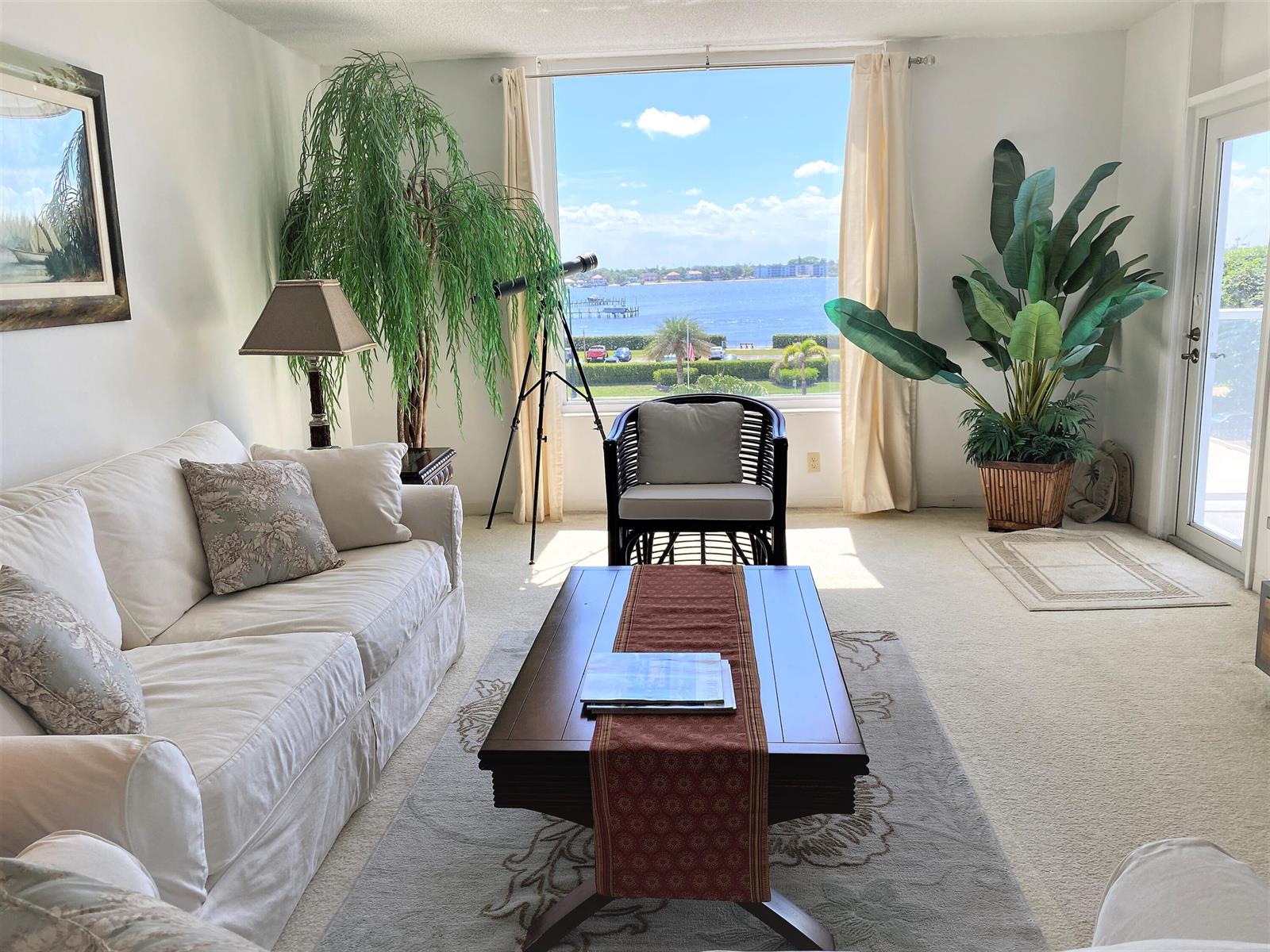 A living room with a white sofa, coffee table, and large window overlooking the water — 3450 S Ocean Boulevard # 3280, Palm Beach FL 33480, PALM BEACH, FL