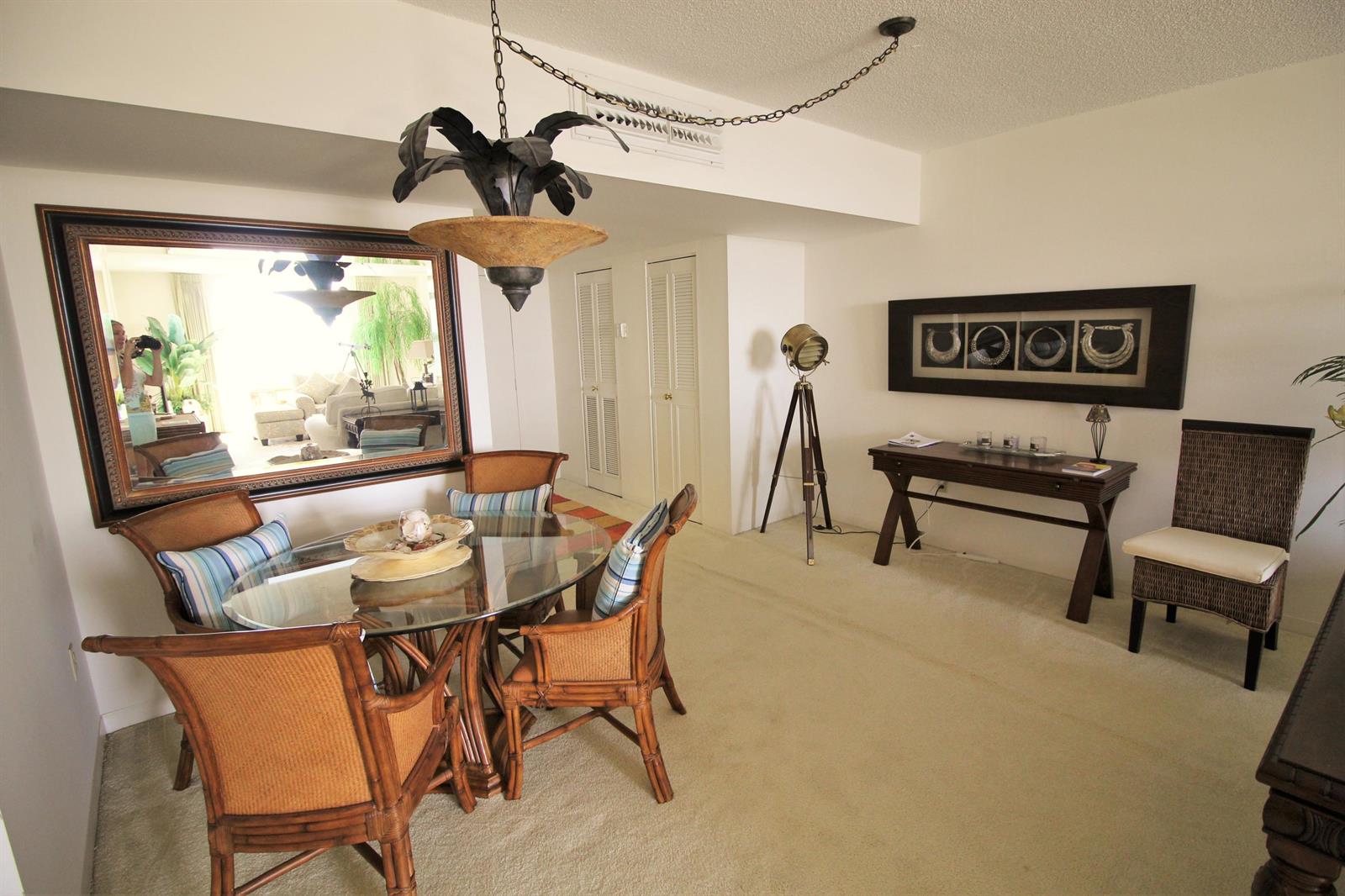 A dining area features a glass-topped rattan table, a large wall mirror, and a tripod lamp — 3450 S Ocean Boulevard # 3280, Palm Beach FL 33480, PALM BEACH, FL