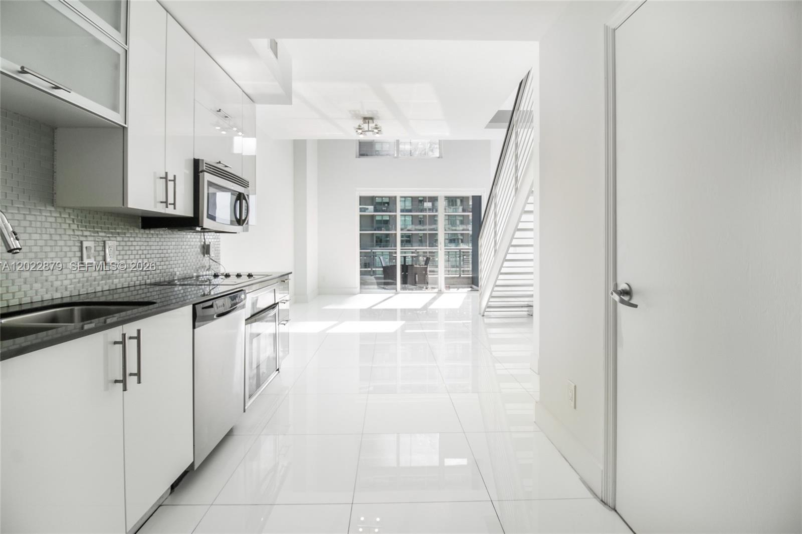 A modern kitchen with white cabinets and black countertops leads to a bright living area — 60 SW 13th St # 2208, Miami FL 33130, MIAMI, FL
