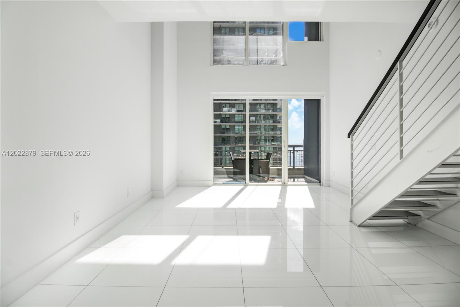 A bright, minimalist living room features white tile floors, high ceilings, and a modern staircase — 60 SW 13th St # 2208, Miami FL 33130, MIAMI, FL