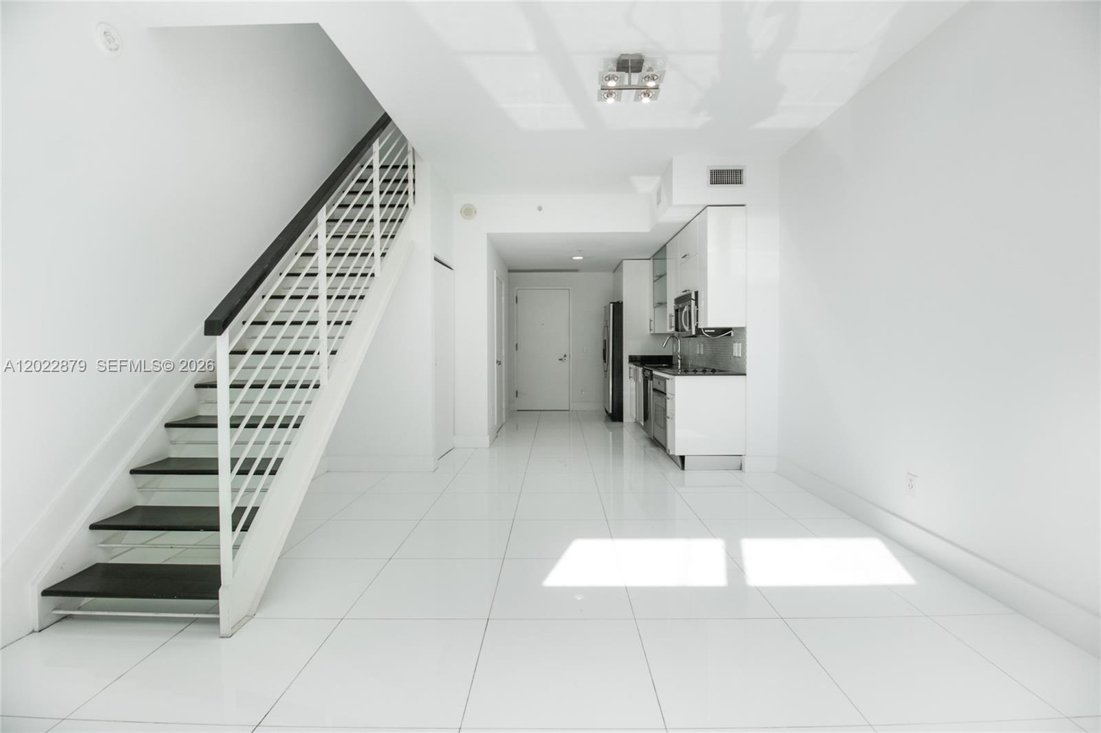 A modern kitchen and living area feature white tile floors and a staircase — 60 SW 13th St # 2208, Miami FL 33130, MIAMI, FL