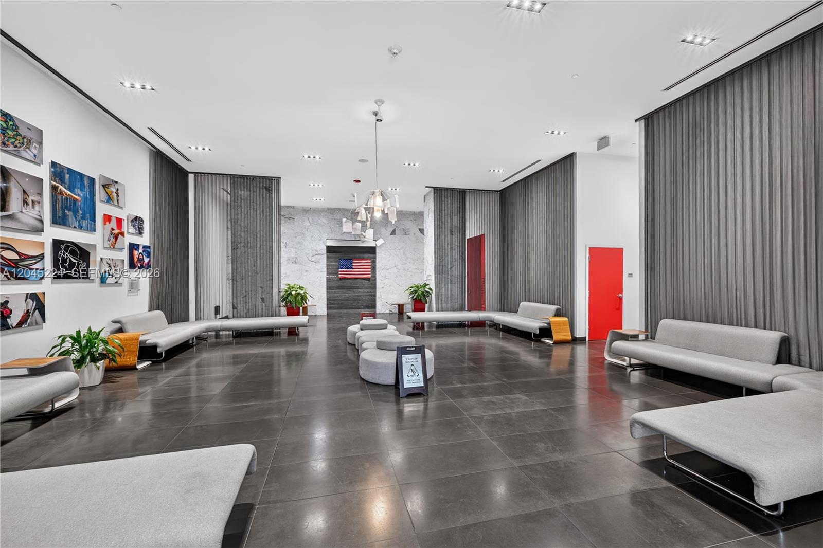 A modern lobby features gray tile floors, minimalist seating, wall art, and a central chandelier — 1600 NE 1st Ave # 1210, Miami FL 33132, MIAMI, FL