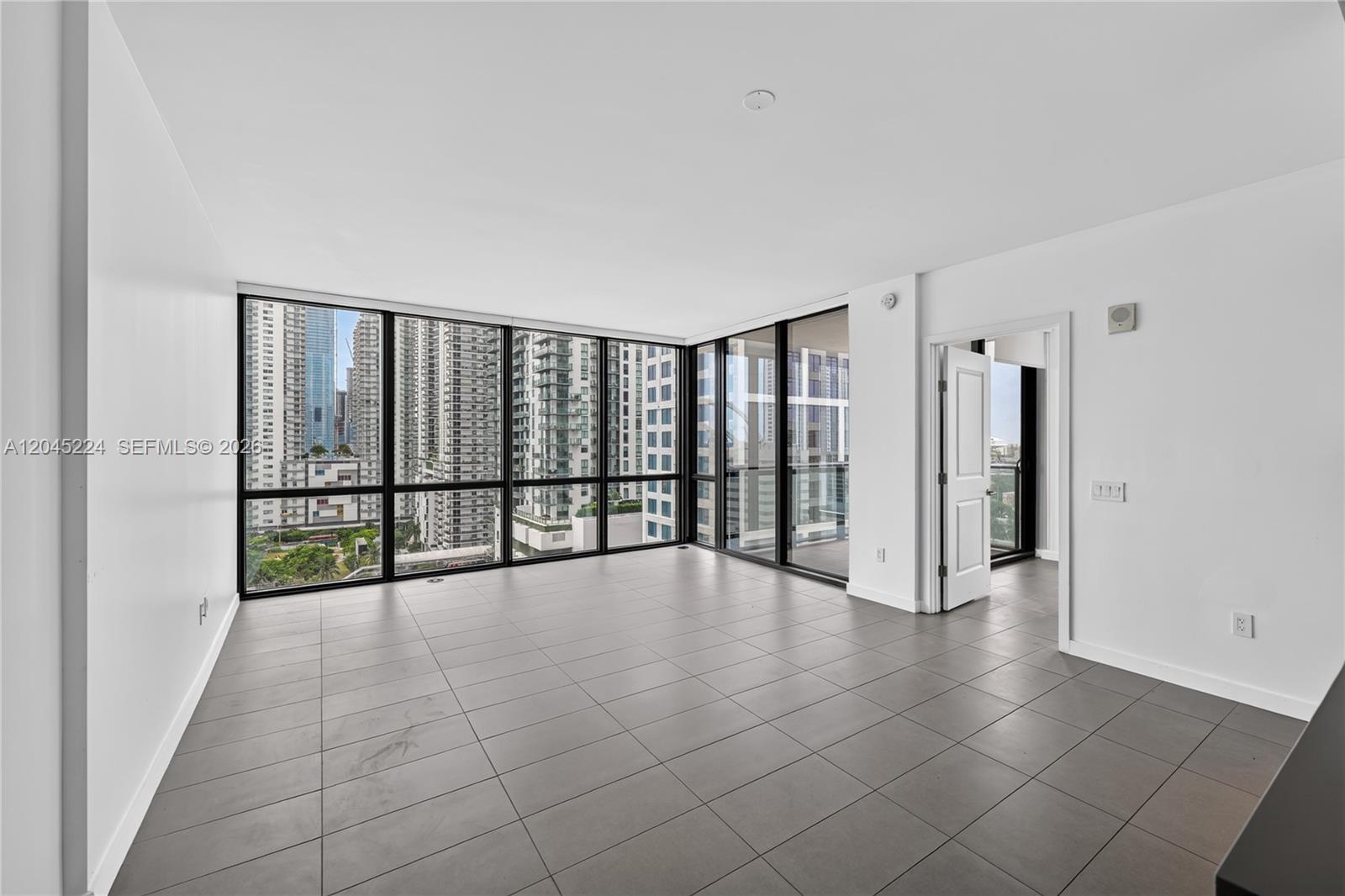 An empty room features large floor-to-ceiling windows, gray tile flooring, and white walls — 1600 NE 1st Ave # 1210, Miami FL 33132, MIAMI, FL