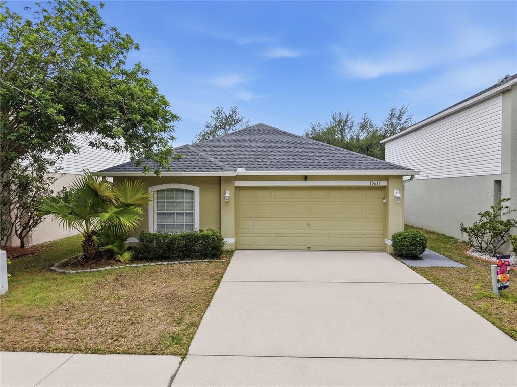 A single-story house with a tan stucco exterior, a two-car garage, and a shingled roof — 10617 OPUS DRIVE, RIVERVIEW, FL