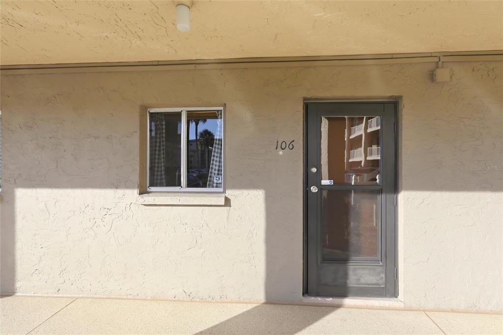 A beige exterior wall features a window and a dark door labeled 106 — 3531 LAKE BAYSHORE DRIVE UNIT J106, BRADENTON, FL