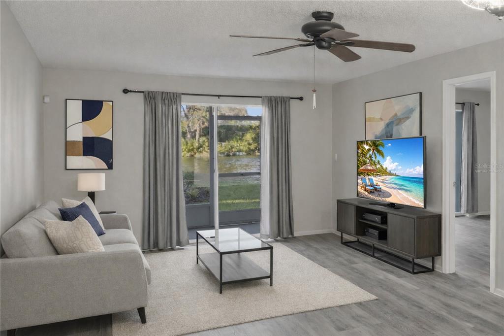 A living room features a gray sofa, glass coffee table, television, and sliding doors to a patio — 3531 LAKE BAYSHORE DRIVE UNIT J106, BRADENTON, FL