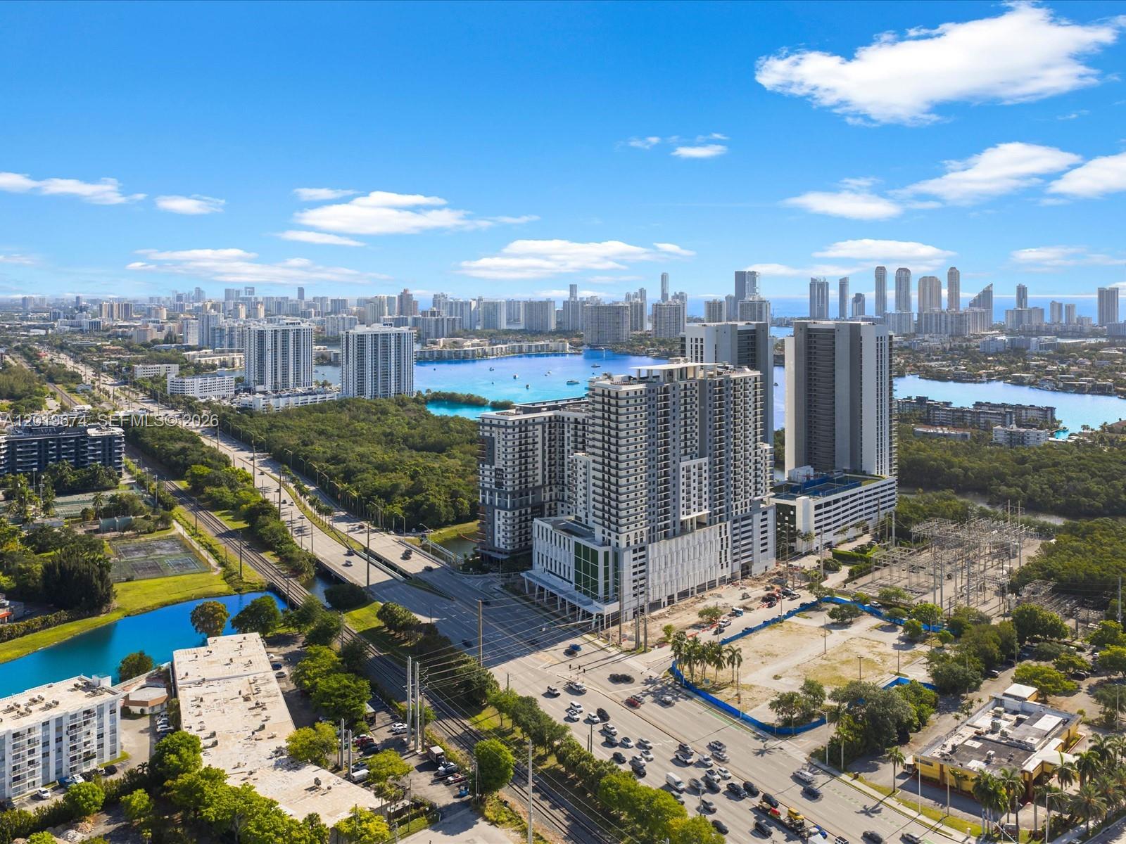 An aerial view shows a modern high-rise building complex surrounded by roads, greenery, and water — 16385 Biscayne Blvd # 3103, North Miami Beach FL 33160, NORTH MIAMI BEACH, FL
