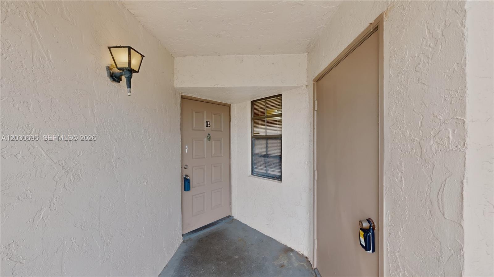 A beige exterior entryway features a door marked E, a window, and a wall lamp — 889 Hamilton Dr # 889E, Homestead FL 33034, HOMESTEAD, FL