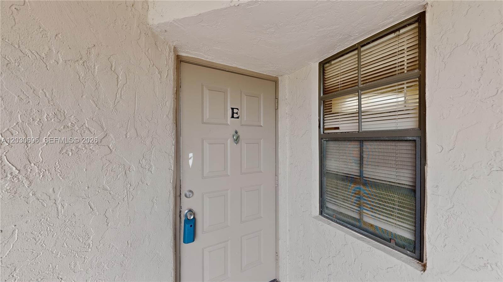 A beige exterior door marked with the letter E sits beside a window with blinds — 889 Hamilton Dr # 889E, Homestead FL 33034, HOMESTEAD, FL