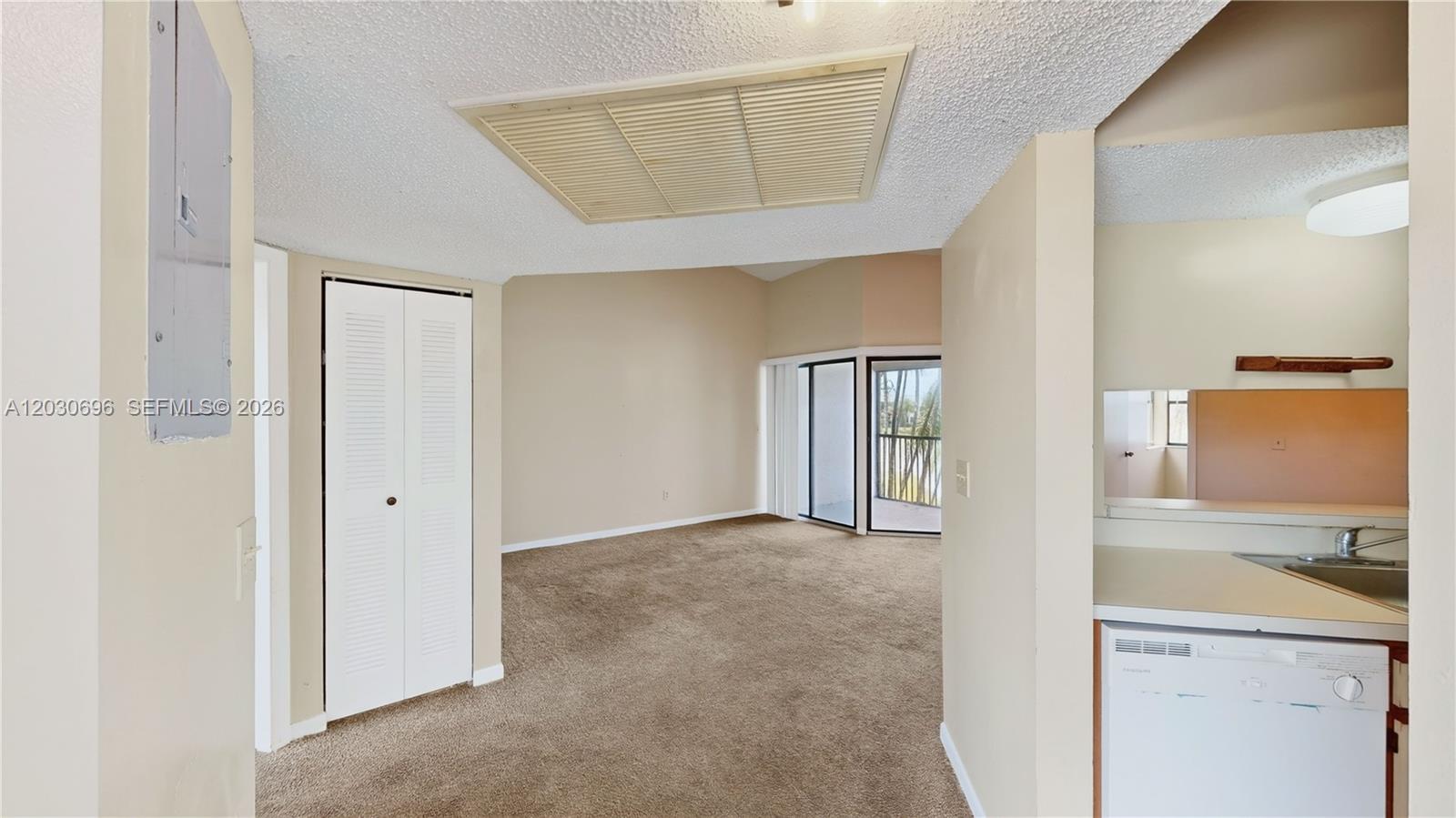 An interior view shows a carpeted living area with a closet and an adjacent kitchen — 889 Hamilton Dr # 889E, Homestead FL 33034, HOMESTEAD, FL