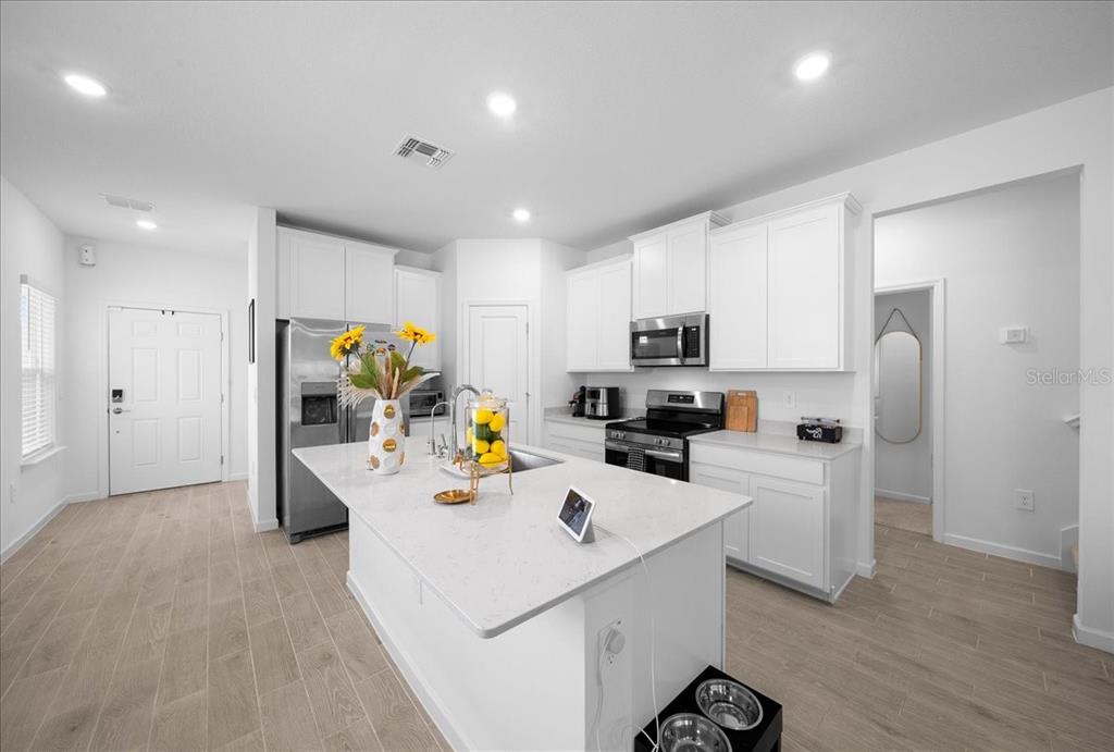 A modern kitchen features white cabinets, a quartz-topped island, and light wood-look tile flooring — 3902 NE 30TH TERRACE, OCALA, FL