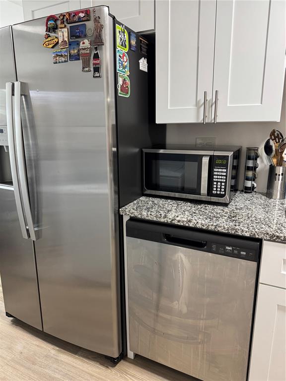 A kitchen features a stainless steel refrigerator, a microwave, and a dishwasher with granite countertops — 2342 BARBADOS COURT, KISSIMMEE, FL