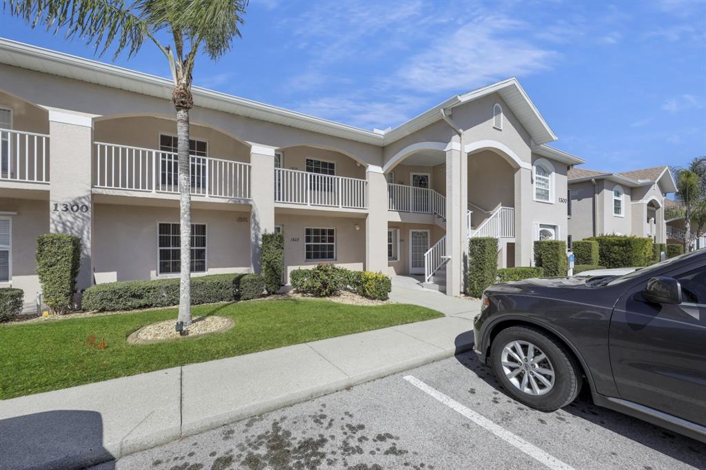 A two-story apartment building with a beige exterior, white railings, and a parking lot — 11644 SW EGRET CIRCLE UNIT 1307, LAKE SUZY, FL
