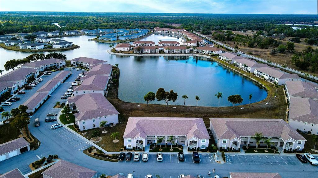 An aerial view shows multiple apartment buildings surrounding a large central lake — 11644 SW EGRET CIRCLE UNIT 1307, LAKE SUZY, FL