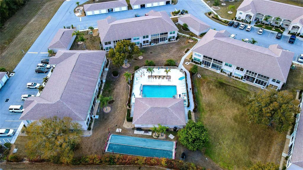 An aerial view shows apartment buildings surrounding a central swimming pool and a tennis court — 11644 SW EGRET CIRCLE UNIT 1307, LAKE SUZY, FL