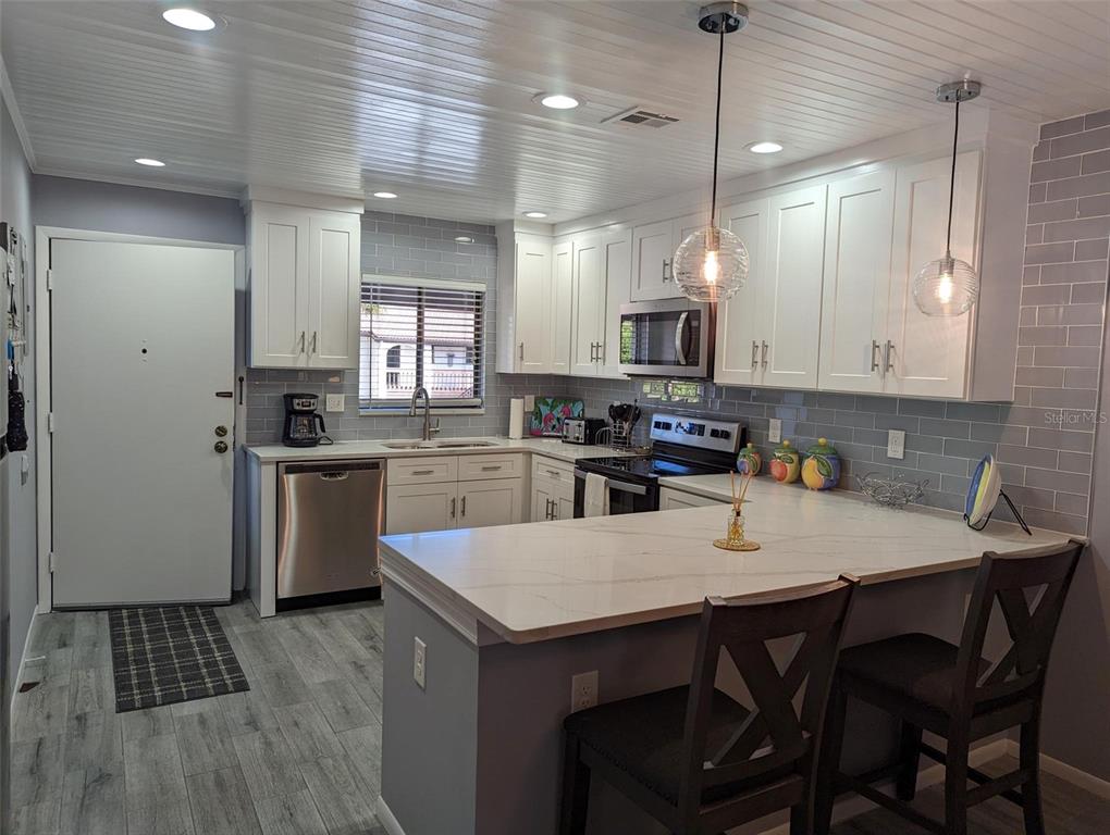A kitchen features white cabinets, gray subway tile backsplash, stainless appliances, and a peninsula counter — 1634 STICKNEY POINT ROAD UNIT 1634-2, SARASOTA, FL