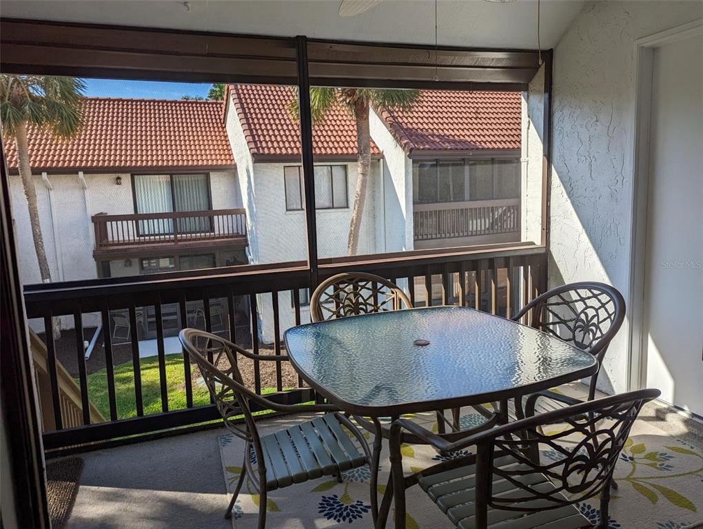 A screened-in balcony features a glass-top table with four chairs overlooking a residential complex — 1634 STICKNEY POINT ROAD UNIT 1634-2, SARASOTA, FL