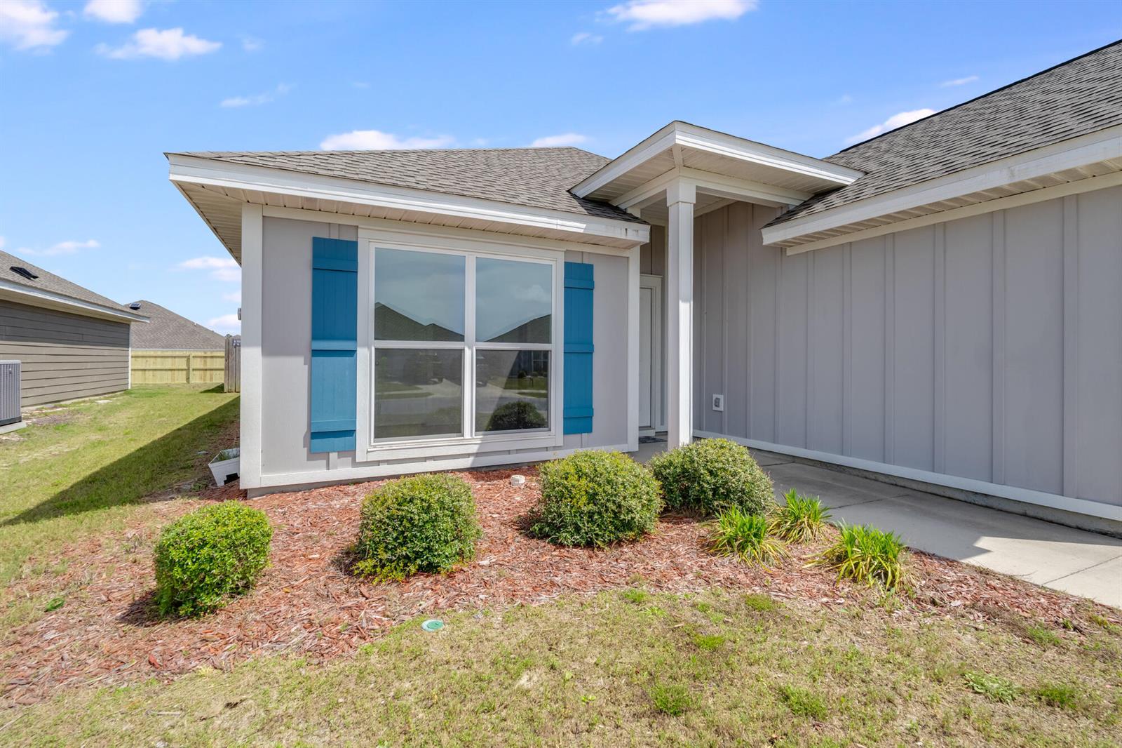The exterior of a gray house features blue shutters, a covered entryway, and landscaping — 274 Bayou Bend Lane, Panama City FL 32404, PANAMA CITY, FL