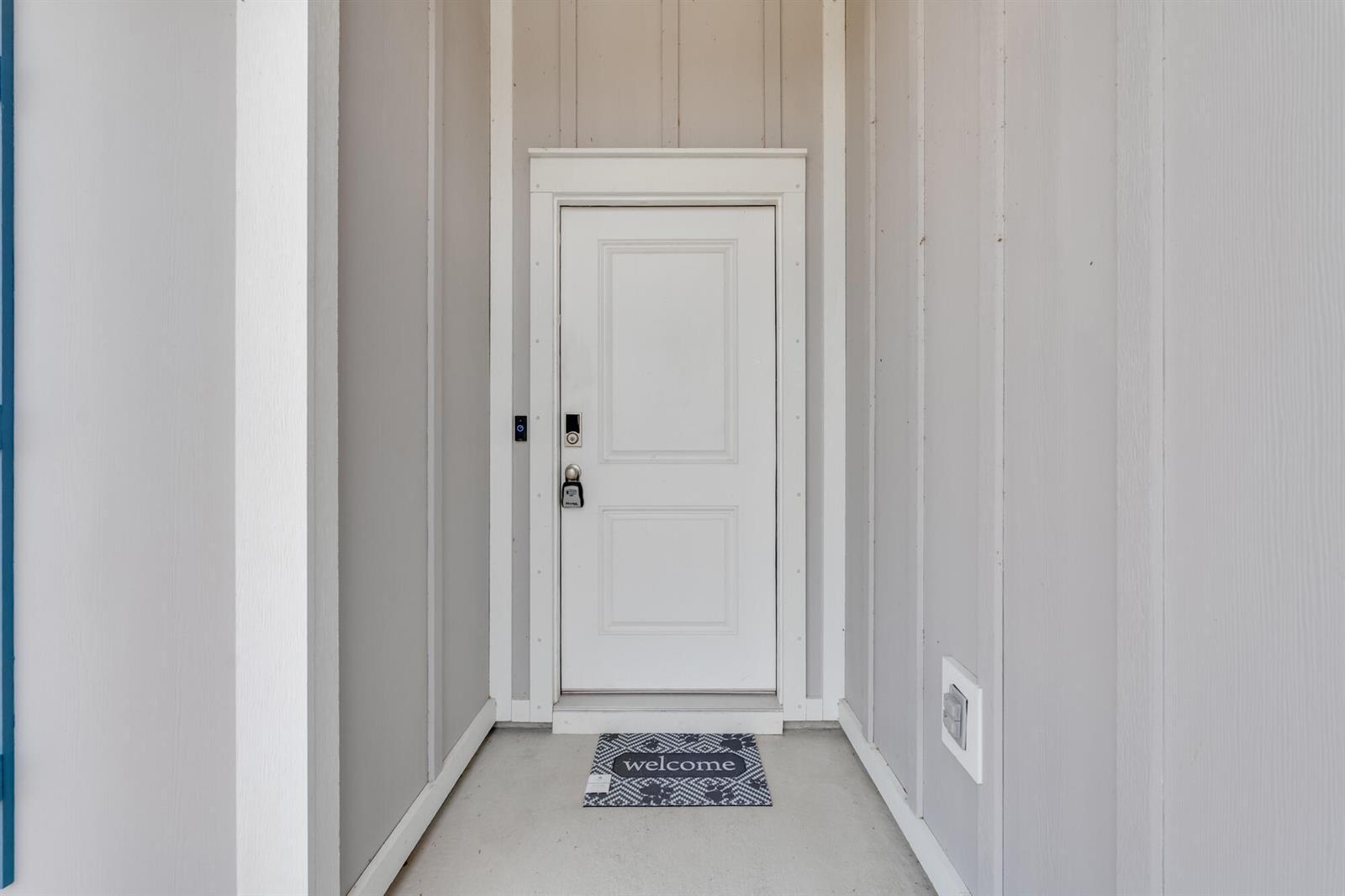 A white front door with a welcome mat is set within a gray-sided entryway — 274 Bayou Bend Lane, Panama City FL 32404, PANAMA CITY, FL