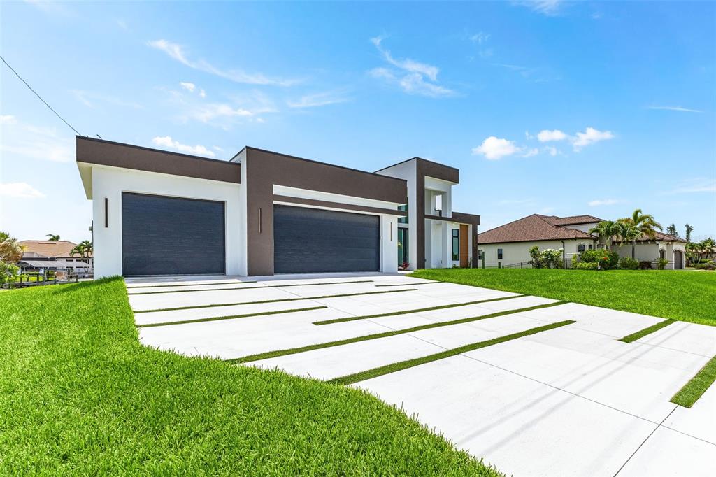 A modern house exterior features a two-car garage and a concrete driveway with grass strips — 1503 NW 38 AVENUE, CAPE CORAL, FL