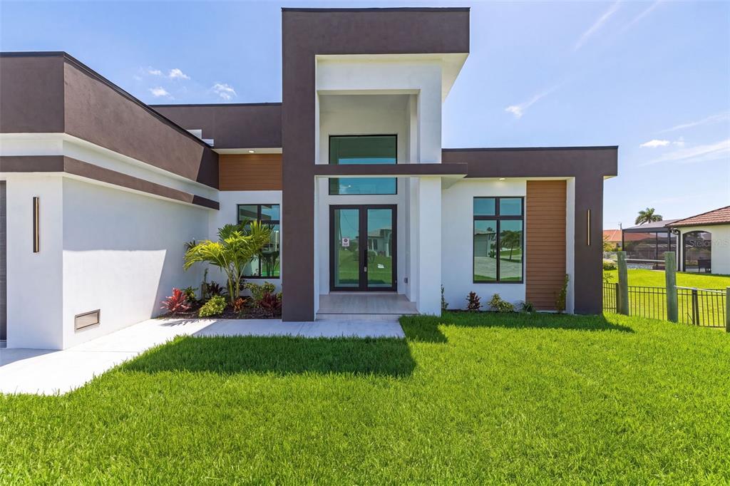 A modern single-story house exterior with dark brown accents, white walls, and a glass entryway — 1503 NW 38 AVENUE, CAPE CORAL, FL