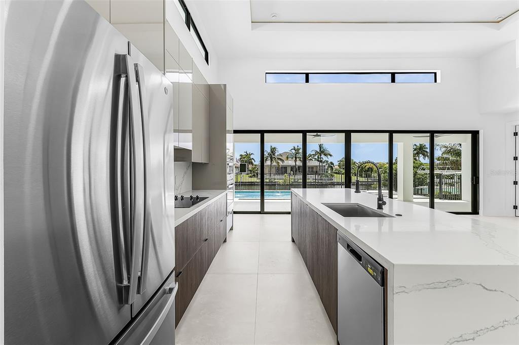 A modern kitchen features a large island, stainless steel appliances, and floor-to-ceiling windows overlooking a pool — 1503 NW 38 AVENUE, CAPE CORAL, FL