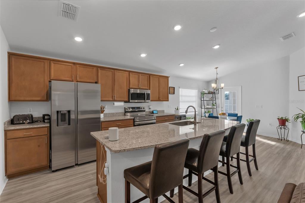 A kitchen features wood cabinets, granite countertops, a stainless steel refrigerator, and a breakfast bar — 4820 SE 91ST PLACE, OCALA, FL
