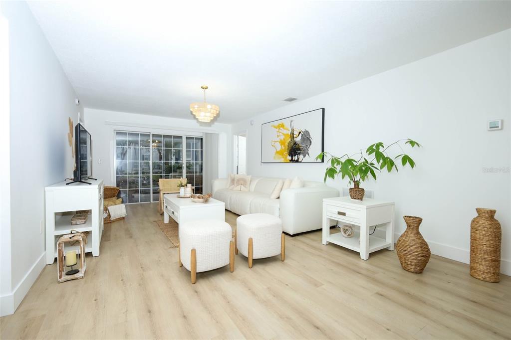 A bright living room features light wood flooring, a white sofa, and a glass sliding door — 7102 OLYMPIA COURT UNIT 7102, LONGWOOD, FL