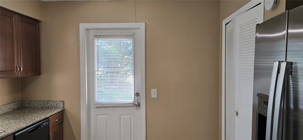 A kitchen features brown cabinets, granite countertops, a white door with blinds, and a refrigerator — 2530 GEORGIA AVENUE UNIT B, SANFORD, FL
