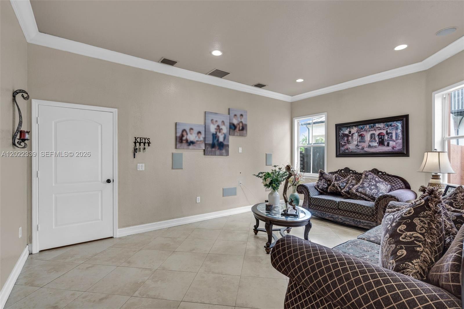 A living room features beige walls, tile flooring, two sofas, and family photos on display — 18122 NW 91st Ct, Hialeah FL 33018, HIALEAH, FL