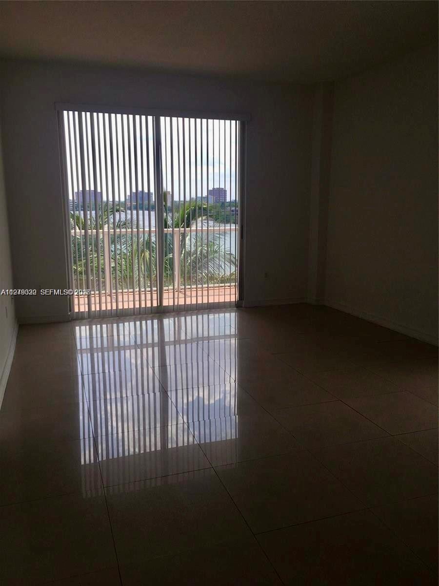 An empty room features light-colored tile flooring and a sliding glass door with vertical blinds — 5091 NW 7th St # 602, Miami FL 33126, MIAMI, FL