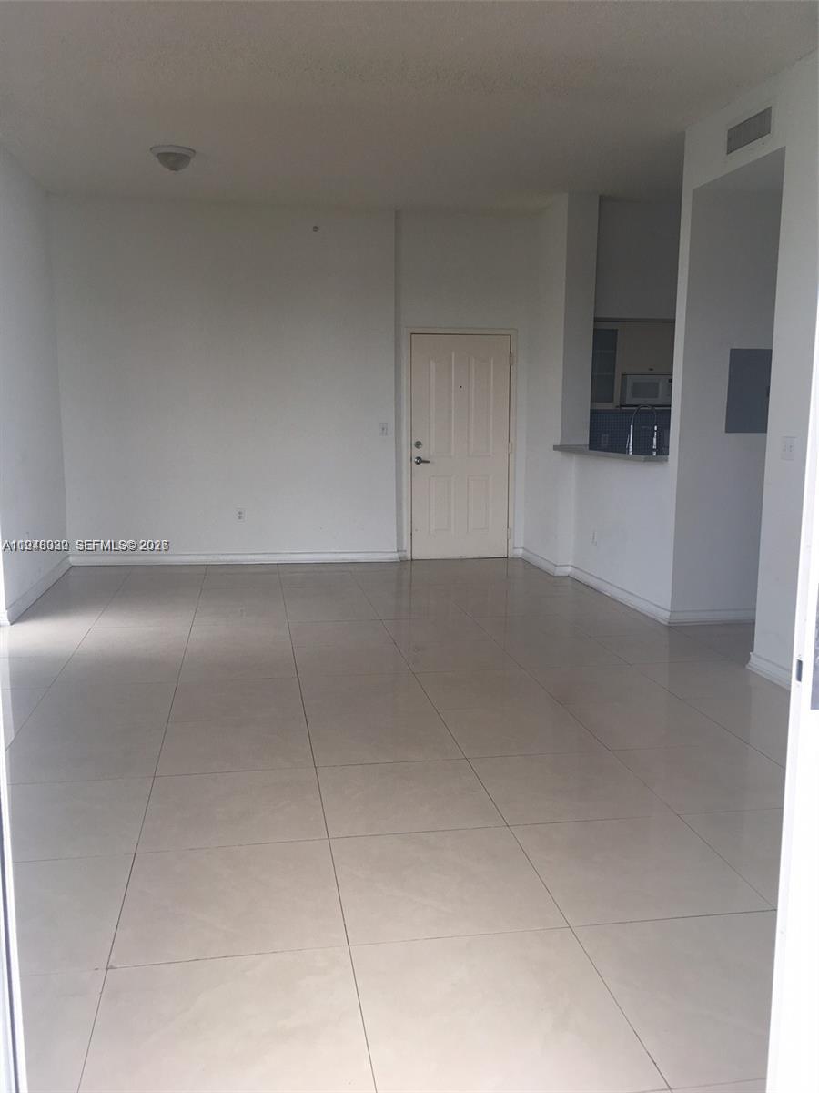 An empty room features white walls, light-colored tile flooring, and an adjacent kitchen area — 5091 NW 7th St # 602, Miami FL 33126, MIAMI, FL